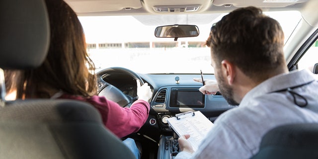 Rear view of mid adult teacher pointing while woman parking car