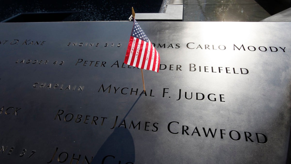 FILE – In this Monday, Sept. 12, 2011 file photo, a U.S. flag is stuck into the etched name of Father Mychal F. Judge, the New York Fire Department chaplain who died in the 9/11 attacks on the World Trade Center, at the National September 11 Memorial in New York. (AP Photo/Mike Segar, Pool, File)