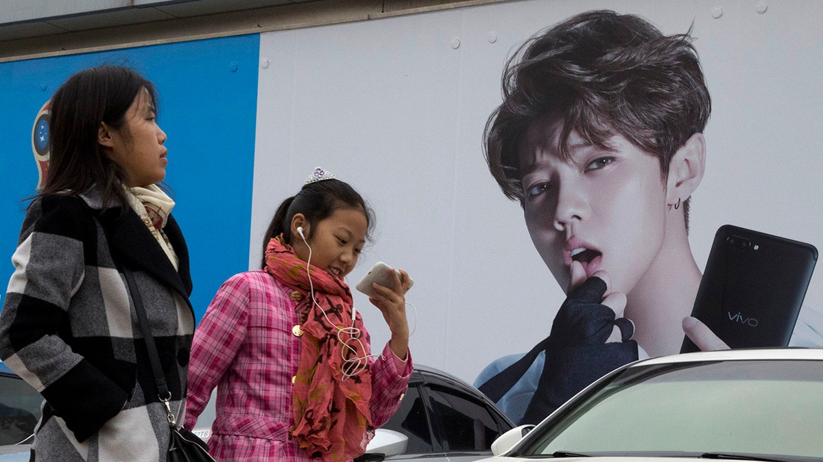 FILE - In this Oct. 21, 2017, file photo, Chinese women walk past advertisement featuring teen idol Lu Han, also known as China's Justin Bieber in Beijing. China's government banned effeminate men on TV and told broadcasters Thursday, Sept. 2, 2021 to promote "revolutionary culture," broadening a campaign to tighten control over business and society and enforce official morality. 
