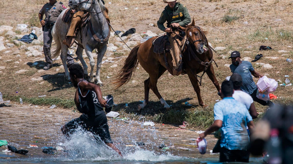Two border patrol agents riding on horses push back a group of Haitian migrants