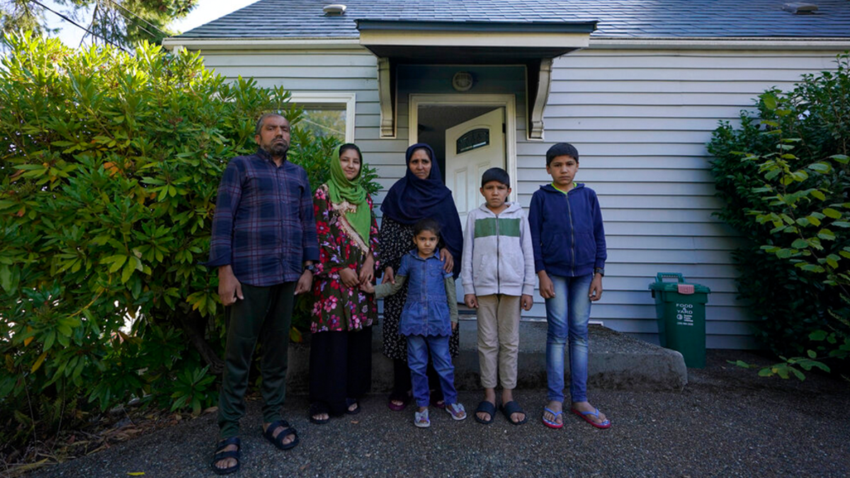 Abdul, left, who worked as a mechanic before he left Kabul, Afghanistan with his family about a month ago, poses for a photo, Thursday, Sept. 16, 2021, with his family in front of a rental house where they have been provided a place to stay in Seattle.
