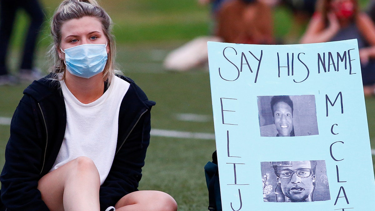 A person sits next to a sign as people gather to commemorate the one-year anniversary of Elijah McClain's death in Denver, Colorado, on Aug. 23, 2020.