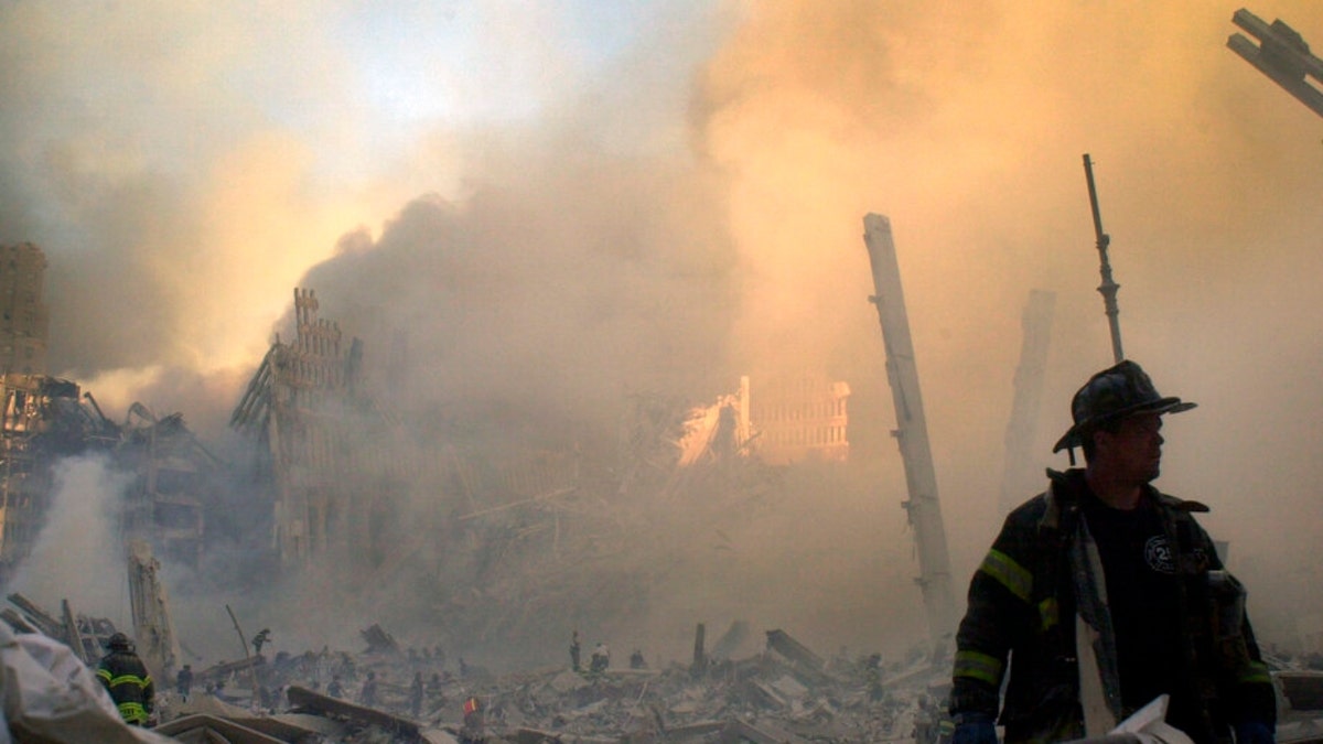 smoke and debris from Ground Zero as firefighter walks in foreground on 9/11/2001