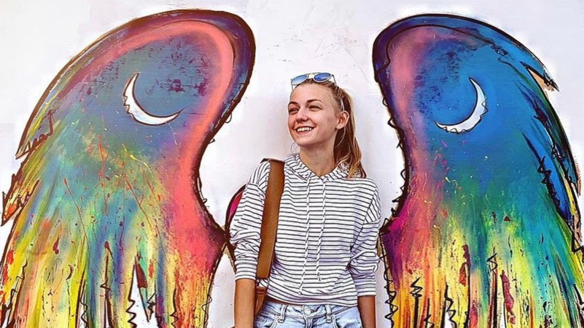 Gabby Petito poses in front of a winged mural