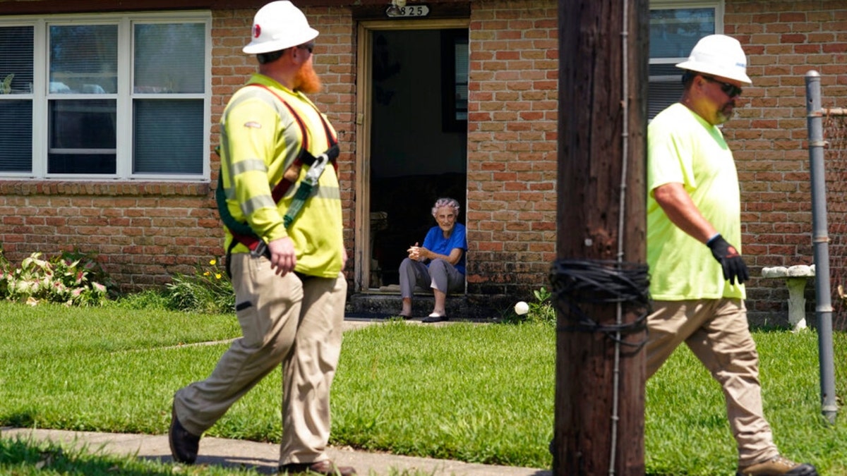 Berth Topolanek, center, who lost power due to Hurricane Ida, watches from her doorstep as energy workers assess and repair lines in her neighborhood, Wednesday, Sept. 1, 2021, in New Orleans, La. Power was restored to an area just blocks away Monday, but some part of New Orleans may be without power for weeks. 