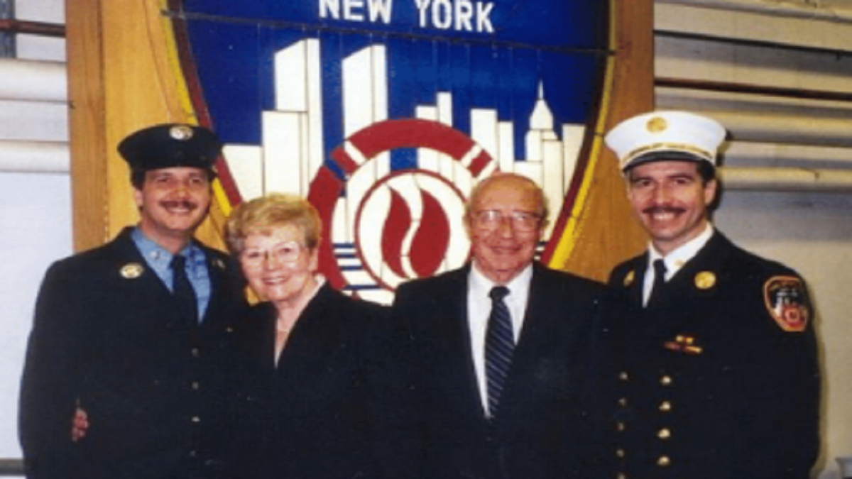 Photograph shows FDNY Battalion Chief Joseph Pfeifer (far right) with his brother, Kevin Pfeifer (far left), celebrating Kevin's promotion to FDNY lieutenant with their parents in 1999