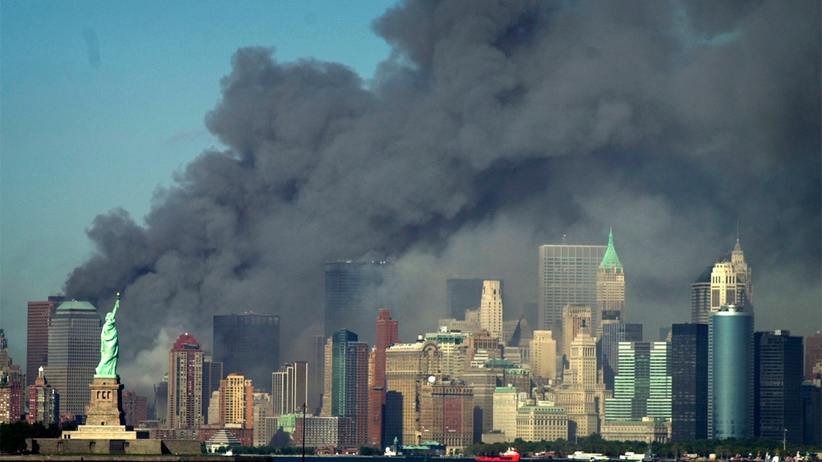 Thick smoke billows into the sky from the area behind the Statue of Liberty, lower left, where the World Trade Center was, on Tuesday, 9/11/01