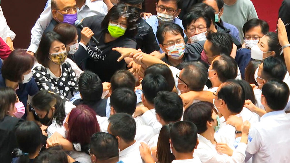 In this image taken from video by Taiwan's EBC, Premier Su Tseng-chang, in purple mask, tries to make a policy speech amid a scuffle between opposition Nationalist party and ruling Democratic Progressive Party lawmakersduring a parliament session in Taipei, Taiwan, Tuesday, Sept. 28, 2021. Taiwan's legislature on Tuesday descended into a rowdy brawl on Tuesday, after opposition lawmakers interrupted an important policy address and rushed the podium. (EBC via AP )