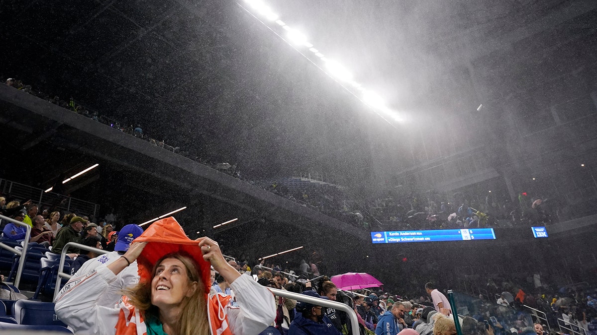 A fan covers herself from rain in Louis Armstrong Stadium during a match between Kevin Anderson, of South Africa, and Diego Schwartzman, of Argentina, in the second round of the US Open tennis championships, Wednesday, Sept. 1, 2021, in New York. (AP Photo/Frank Franklin II)