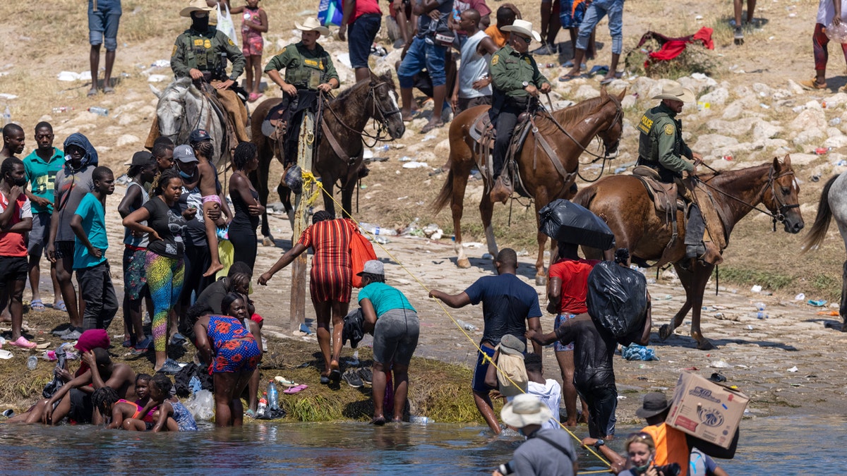 Mounted U.S. Border Patrol agents watch Haitian immigrants on the bank of the Rio Grande in Del Rio, Texas, on Sept. 20, 2021, as seen from Ciudad Acuna, Mexico.