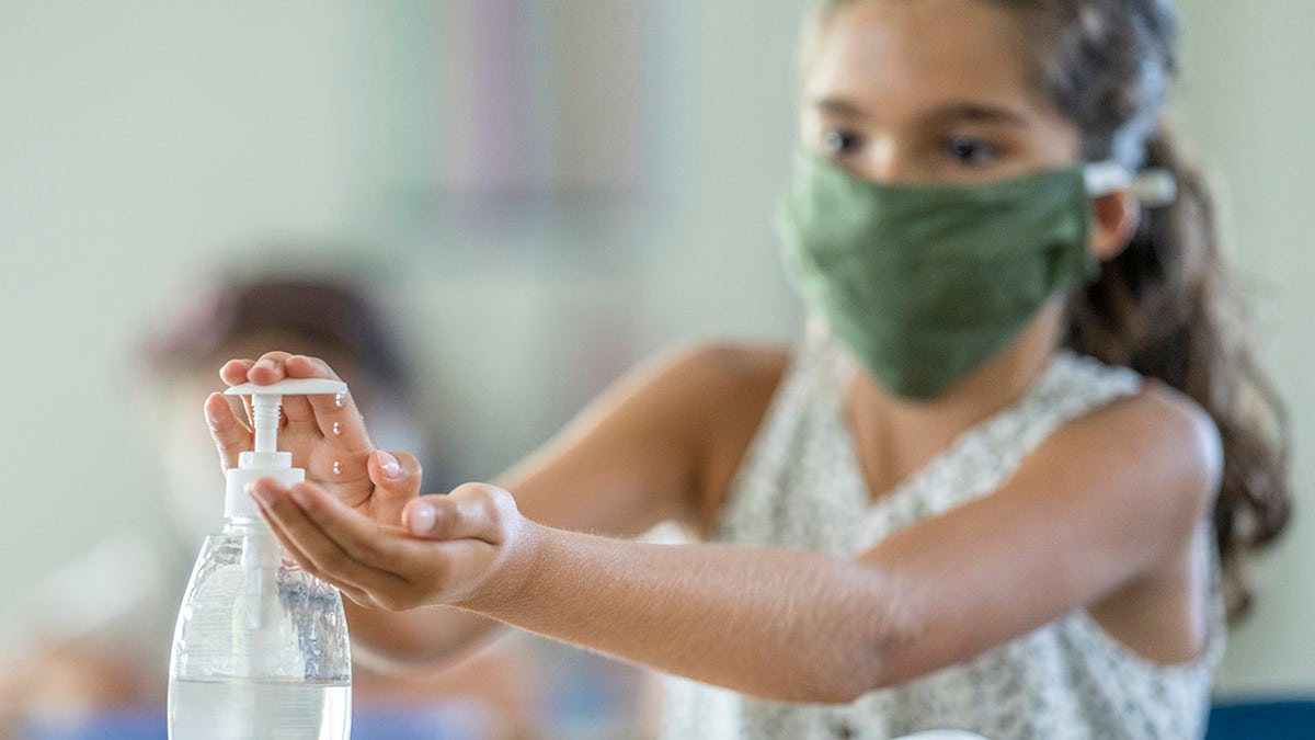 12 year old student using hand sanitizer in class while wearing a protective face mask to avoid the transfer of germs during the reopening of schools because of COVID-19.