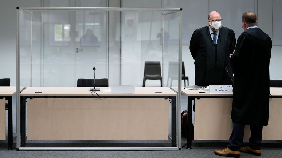 Two lawmakers stand next to an empty seat of the accused at the courtroom, prior to a trial against a 96-year-old former secretary for the SS commander of the Stutthof concentration camp at the court in Itzehoe, Germany, Thursday, Sept. 30, 2021. The woman is charged of more than 11,000 counts of accessory to murder. Prosecutors argue that the 96-year-old woman was part of the apparatus that helped the Nazi camp function more than 75 years ago.(AP Photo/Markus Schreiber, Pool)