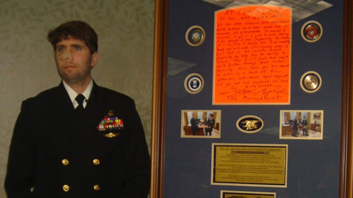 Jason Redman stands in uniform beside the sign that was posted outside his hospital room.