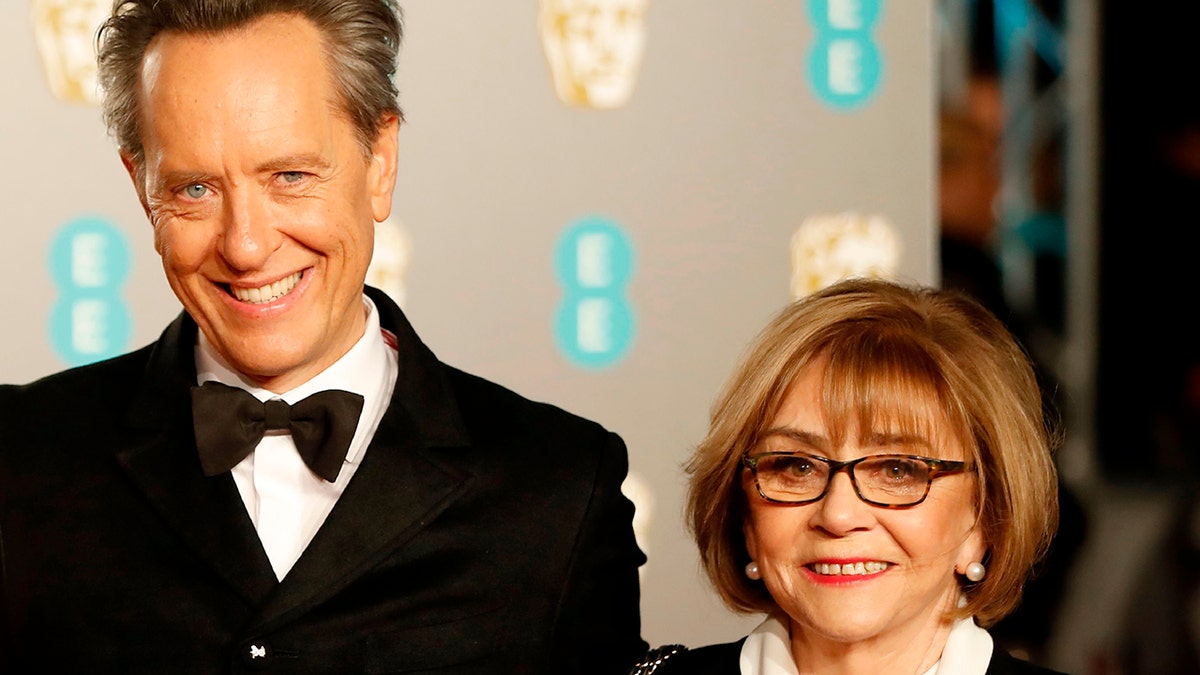British actor Richard E. Grant (C) poses on the red carpet with his wife Joan Washington (R) upon arrival at the BAFTA British Academy Film Awards at the Royal Albert Hall in London on February 10, 2019. 