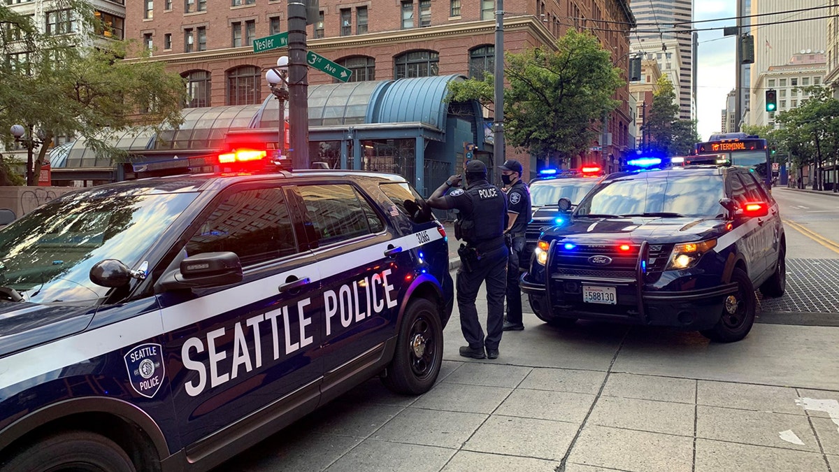 Photo shows Seattle police vehicles with lights on and officers standing near the cars at a crime scene in 2021