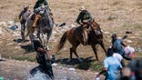 Two border patrol agents riding on horses push back a group of Haitian migrants