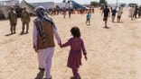 A man walks with a child through Fort Bliss' Doña Ana Village where Afghan refugees are being housed, in New Mexico, Friday, Sept. 10, 2021. The Biden administration provided the first public look inside the U.S. military base where Afghans airlifted out of Afghanistan are screened, amid questions about how the government is caring for the refugees and vetting them. (AP Photo/David Goldman)