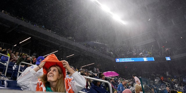 Фанатка прикрывается от дождя на стадионе Луи Армстронга в Квинсе, штат Нью-Йорк, на открытом чемпионате США по теннису, 1 сентября 2021 года.  (Associated Press)