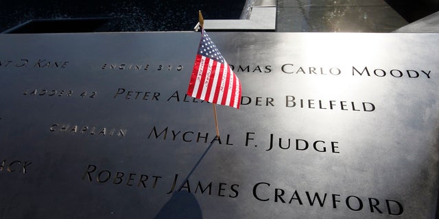 FILE – In this Monday, Sept. 12, 2011 file photo, a U.S. flag is stuck into the etched name of Father Mychal F. Judge, the New York Fire Department chaplain who died in the 9/11 attacks on the World Trade Center, at the National September 11 Memorial in New York. (AP Photo/Mike Segar, Pool, File)