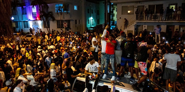  In this March 21,file photo, crowds defiantly gather in the street while a speaker blasts music an hour past curfew in Miami Beach, Fla.