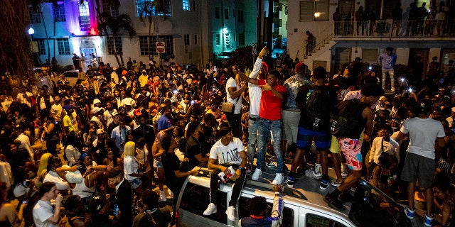  In this March 21,file photo, crowds defiantly gather in the street while a speaker blasts music an hour past curfew in Miami Beach, Fla.