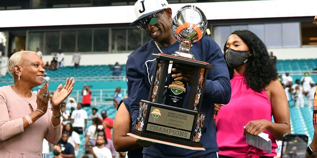 Jackson State head football coach Deion Sanders, center, holds the Orange Blossom Classic trophy after winning an NCAA college football game over Florida A&M, Sunday, Sept. 5, 2021, in Miami Gardens, Fla.