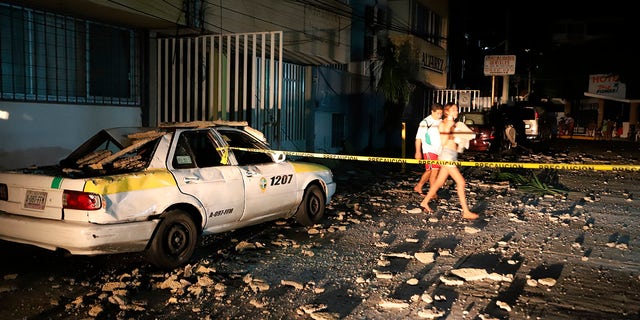 A couple walks past a taxi cab that was damaged by falling debris after a strong earthquake in Acapulco, Mexico, Tuesday, Sept. 7, 2021. (AP Photo/ Bernardino Hernandez)