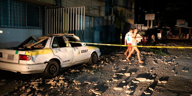 A couple walks past a taxi cab that was damaged by falling debris after a strong earthquake in Acapulco, Mexico, Tuesday, Sept. 7, 2021. (AP Photo/ Bernardino Hernandez)