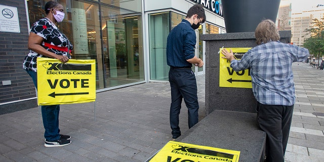 Elections Canada workers place signage at the Halifax Convention Centre as they prepare for the polls to open in the federal election in Halifax on Monday, Sept. 20, 2021.  (Andrew Vaughan/The Canadian Press via AP)