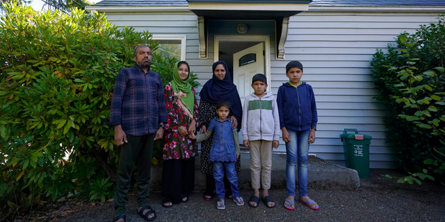 Abdul, left, who worked as a mechanic before he left Kabul, Afghanistan with his family about a month ago, poses for a photo, Thursday, Sept. 16, 2021, with his family in front of a rental house where they have been provided a place to stay in Seattle.
