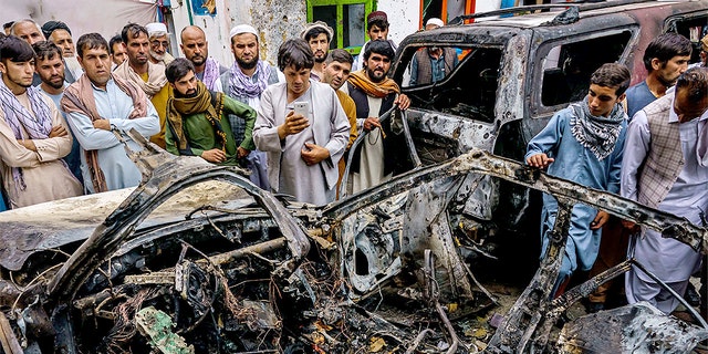 KABUL, AFGHANISTAN -- AUGUST 30, 2021: Relatives and neighbors of the Ahmadi family gathered around the incinerated husk of a vehicle targeted and hit earlier Sunday afternoon by an American drone strike, in Kabul, Afghanistan, Monday, Aug. 30, 2021. (MARCUS YAM / LOS ANGELES TIMES)