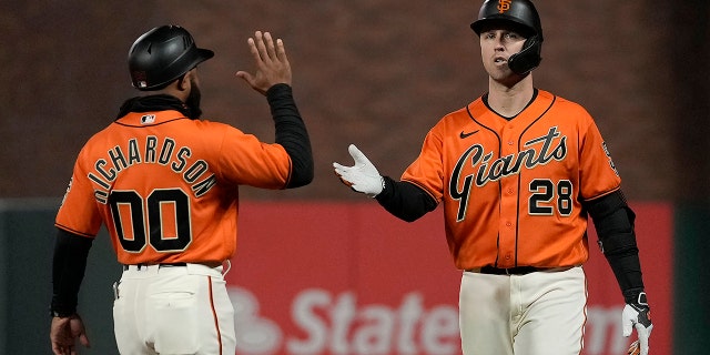 San Francisco Giant Buster Posey (28) is congratulated by first base coach Antoan Richardson (00) after beating a throw to first base against the Los Angeles Dodgers during the 11th inning of a game Friday, 9月. 3, 2021, in San Francisco.
