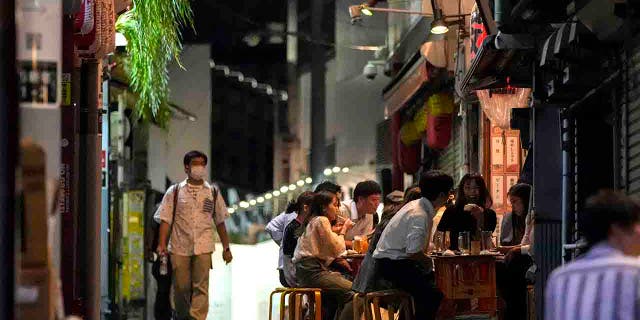 People gather at bars that are open and serving alcohol on an ally filled with bars and restaurants.