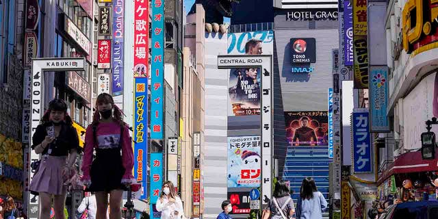 FILE - In this Sept. 20, 2021, file photo, people wearing face masks to help protect against COVID-19 walk past a crossing in Shinjuku, an entertainment district of Tokyo.