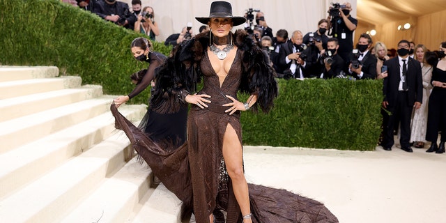 Jennifer Lopez goes with the cowboy hat and Western look in a flowing brown gown with a high-thigh slit and an elegant train.