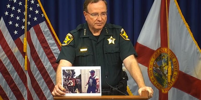 In a Sept. 9, 2021, briefing, Polk County Sheriff Grady Judd holds photos of Bryan Riley, who is accused of killing four people in Lakeland, Florida. 