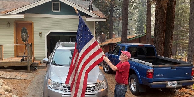 Bill Roberts rolls up an American flag in front of his house in South Lake Tahoe, Calif., last Tuesday -- a day after the city was ordered to evacuate because of the approaching Caldor Fire.   