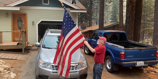 Bill Roberts rolls up an American flag in front of his house in South Lake Tahoe, カリフォルニア, last Tuesday -- a day after the city was ordered to evacuate because of the approaching Caldor Fire.