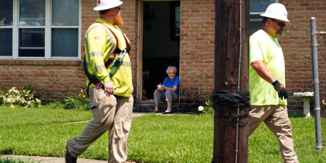 Berth Topolanek, center, who lost power due to Hurricane Ida, watches from her doorstep as energy workers assess and repair lines in her neighborhood, Wednesday, Sept. 1, 2021, in New Orleans, La. Power was restored to an area just blocks away Monday, but some part of New Orleans may be without power for weeks.