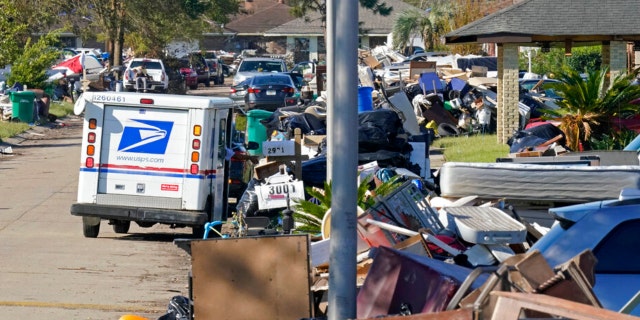 A postal employee delivers mail amidst debris from gutted homes in the aftermath of Hurricane Ida in LaPlace, La., Friday, Sept. 10, 2021.