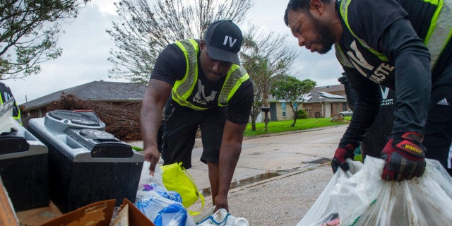 Elmor Garcia and Bruce Hayes, left, of IV Waste, pick up trash and storm debris following Hurricane Ida in Kenner, La., Monday, Sept. 6, 2021.
