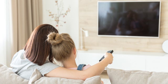 Mother and daughter sitting on sofa watching tv, back view