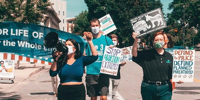 Pro-life Democrats protest at the DNC in 2020. Terrisa Bukovinac shouts in a microphone with Matt Tuman, board chair of Democrats for Life of America, marching behind her and Herb Geraghty, executive director of Rehumanize International, at the right.