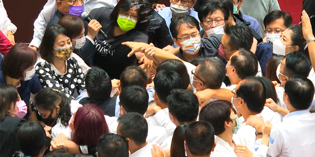 In this image taken from video by Taiwan's EBC, Premier Su Tseng-chang, in purple mask, tries to make a policy speech amid a scuffle between opposition Nationalist party and ruling Democratic Progressive Party lawmakersduring a parliament session in Taipei, Taiwan, Tuesday, Sept. 28, 2021. Taiwan's legislature on Tuesday descended into a rowdy brawl on Tuesday, after opposition lawmakers interrupted an important policy address and rushed the podium. (EBC via AP )