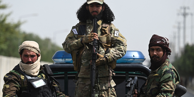 Armed Taliban fighters stand guard atop a vehicle as veiled women march during a pro-Taliban rally outside Shaheed Rabbani Education University in Kabul on September 11, 2021. 