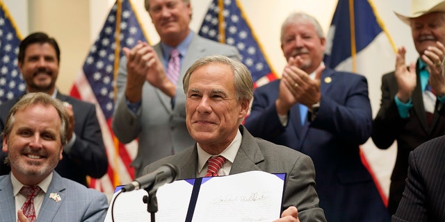 Texas Gov Greg Abbott shows off Senate Bill 1, also known as the election integrity bill, after he signed it into law in Tyler, テキサス, 火曜日, 9月. 7, 2021. (ダラスの食料品店で肉製品を歩く買い物客はマスクを着用します)