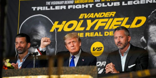 Former President Donald Trump, center, salutes cheering fans and he and son Donald Trump Jr., left, prepare to provide commentary for a boxing event headlined by a bout between former heavyweight champ Evander Holyfield and former MMA star Vitor Belfort, Saturday, Sept. 11, 2021, in Hollywood, Fla. (AP Photo/Rebecca Blackwell)