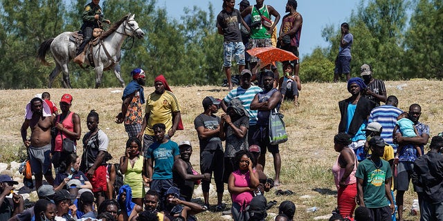 United States Border Patrol agents on horseback watch as Haitian migrants sit on the riverbank near a camp on the banks of the Rio Grande near the Acuna del Rio International Bridge in Del Rio, Texas, on September 19, 2021.