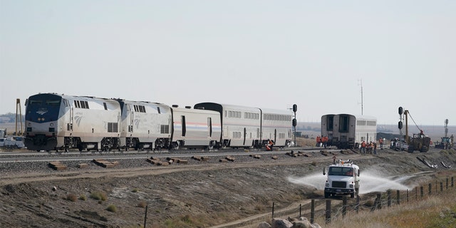 A water truck drives on a road, Monday, Sept. 27, 2021, next to an Amtrak train that derailed Saturday, near Joplin, Mont., killing three people and injuring others. 