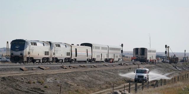 A water truck drives on a road, Monday, Sept. 27, 2021, next to an Amtrak train that derailed Saturday, near Joplin, Mont., killing three people and injuring others.